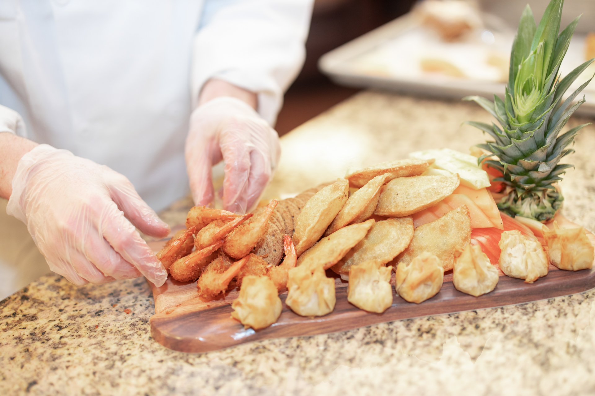 A chef is preparing a board of food decorated with pineapple, shrimp, and wontons