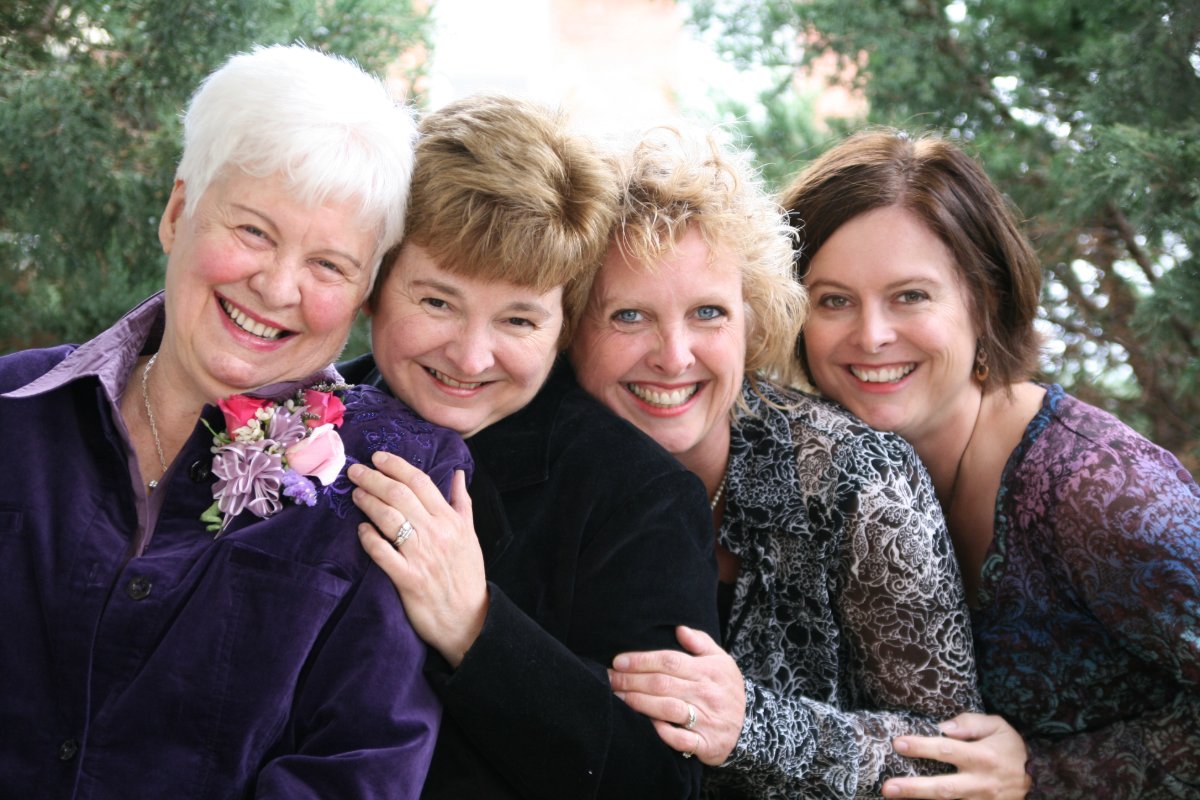 A close-up of 4 women outside holding on to each other arms