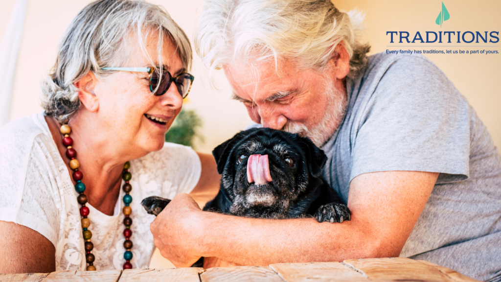 An elderly couple sitting beside each other with a man hugging a black pug. Traditions Management logo in the top right corner.