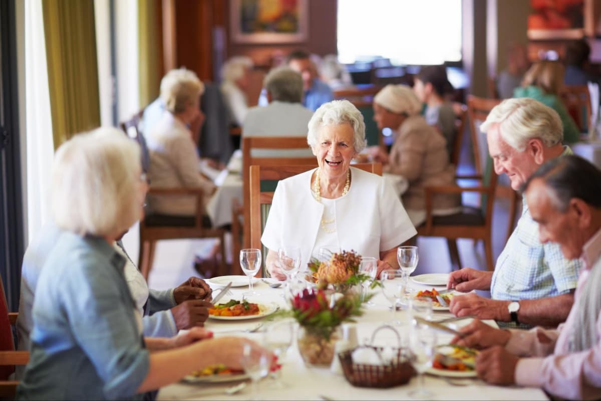 A group of senior men and women sitting at a dining table eating dinner at a senior living facility